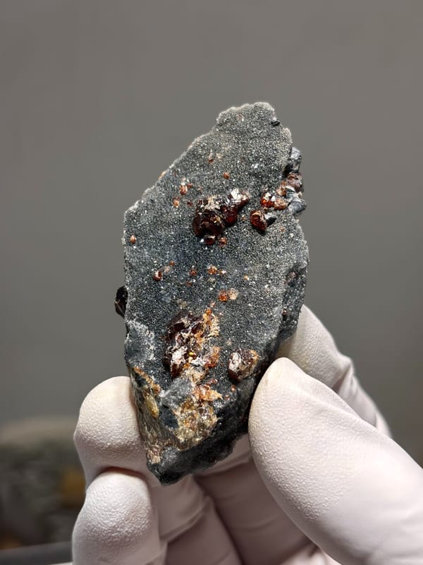 Red-brown sphalerite crystals on grey plate from Hebei, China, held in gloved hand