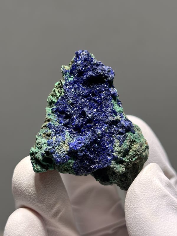 Sparkling azurite crust with green malachite from Hubei, China, held in gloved hand
