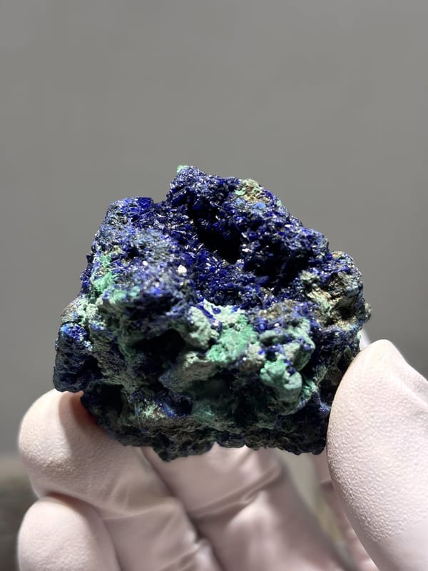 Sparkling azurite nodule with green malachite from Hubei, China, held in gloved hand