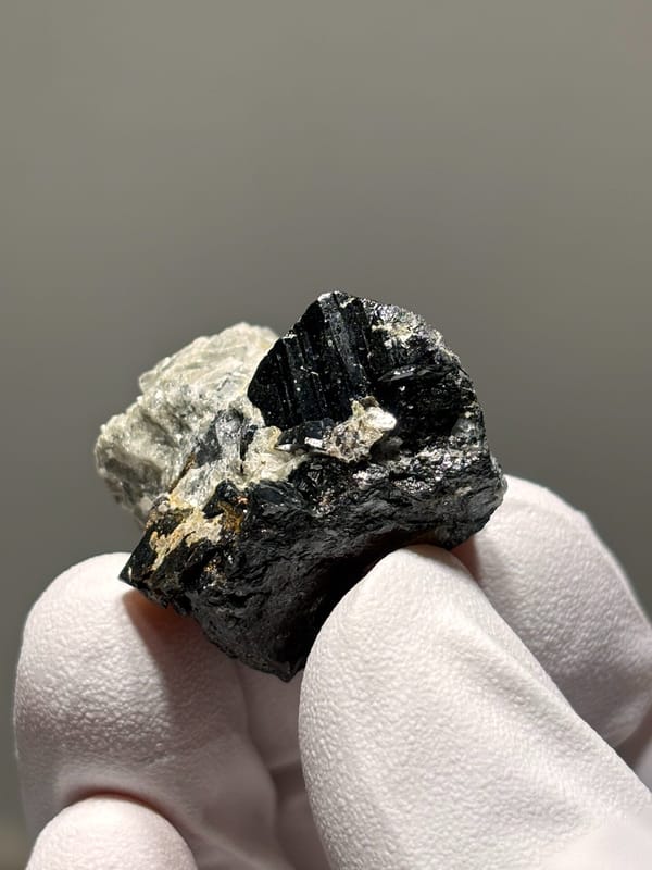 Black cassiterite block with silver mica from Xuebaoding, Sichuan, China, held in gloved hand