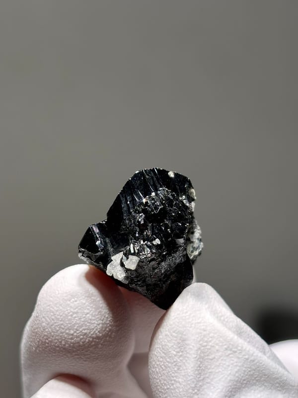 Tiny black cassiterite crystal with white flecks from Xuebaoding, Sichuan, China, close-up of the crystal faces
