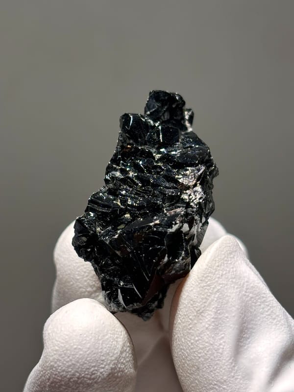 Black cassiterite crystal group from Xuebaoding, Sichuan, China, held in gloved hand