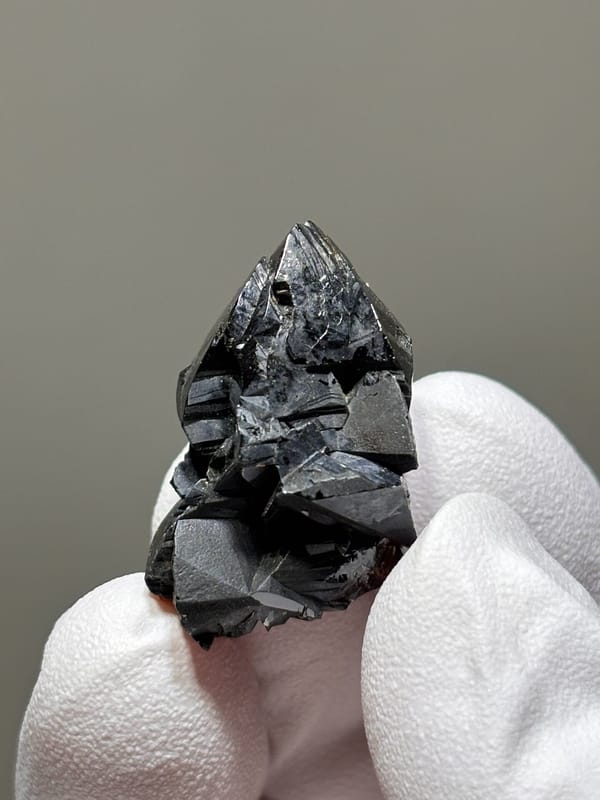 Sharp black cassiterite crystal group from Xuebaoding, Sichuan, China, held in gloved hand