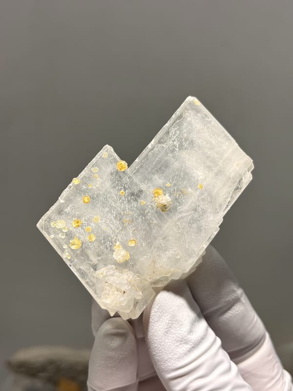Clear baryte blade with yellow calcite specks from Sichuan, China, held in gloved hand