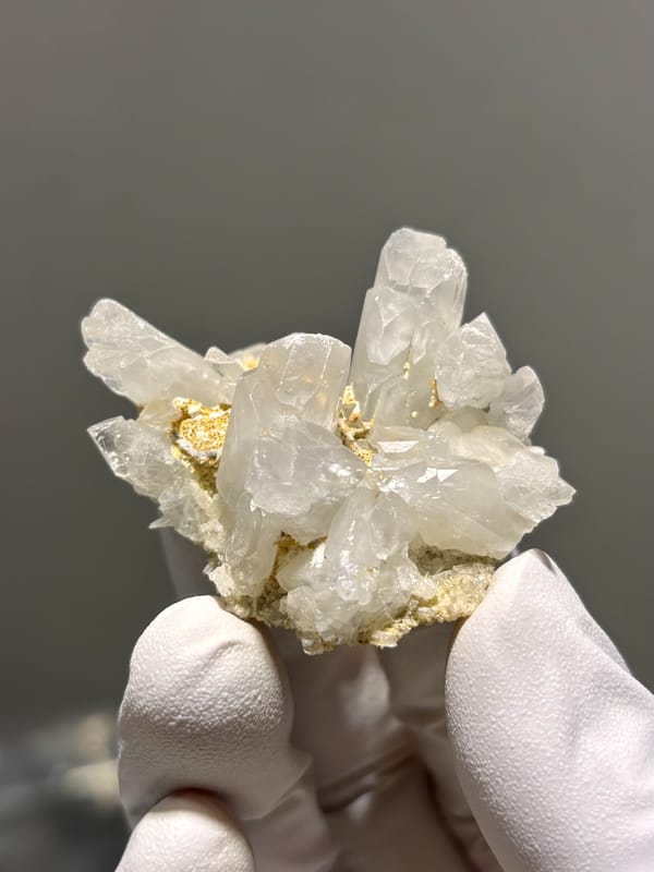 Cluster of clear baryte blades with golden staining from Sichuan, China, held in gloved hand