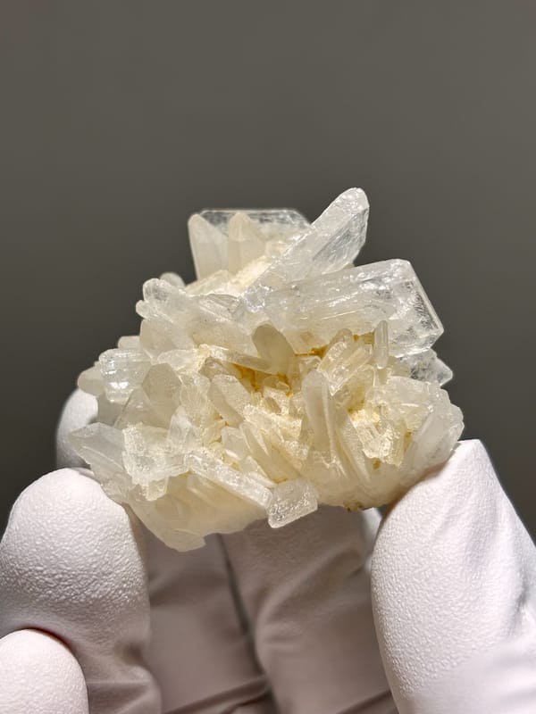 Cluster of cream baryte crystals from Sichuan, China, held in gloved hand