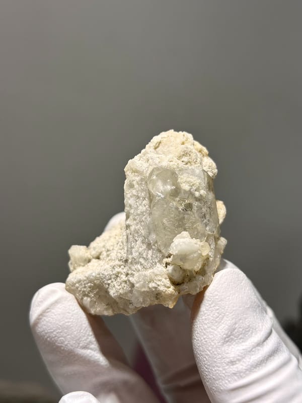Cream baryte crystal in sandy matrix from Sichuan, China, held in gloved hand
