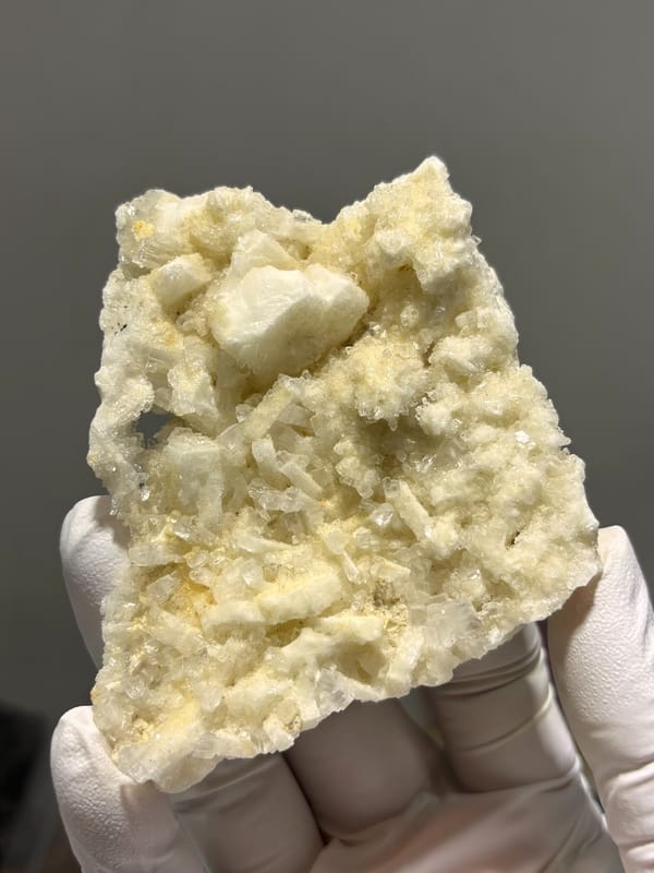 Plate of cream baryte in two crystal habits from Sichuan, China, held in gloved hand