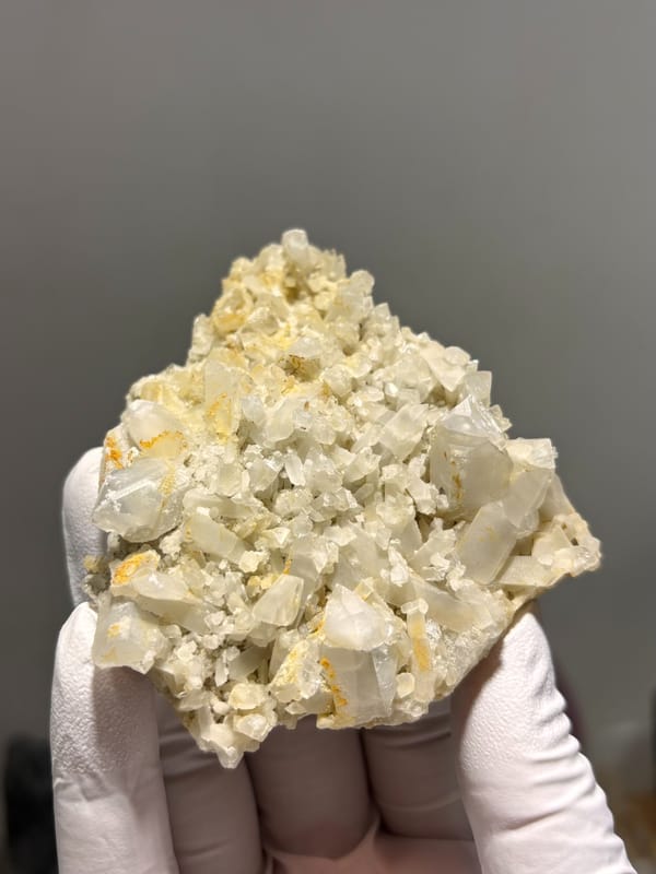Plate of cream baryte crystals with golden staining from Sichuan, China, held in gloved hand