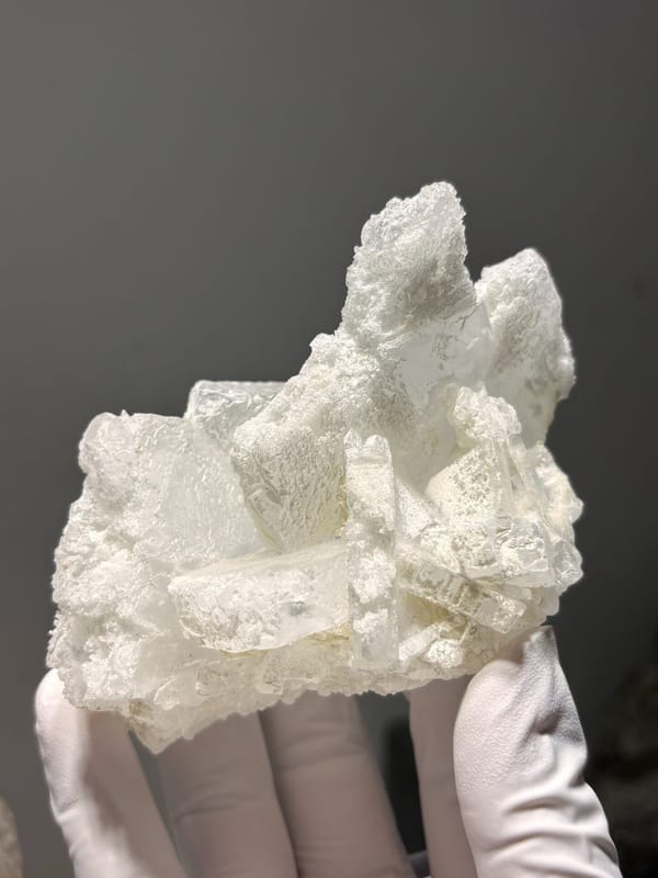 Etched white baryte cluster from Sichuan, China, held in gloved hand