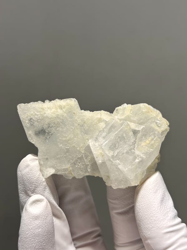 Pale etched baryte crystal group from Sichuan, China, held in gloved hand