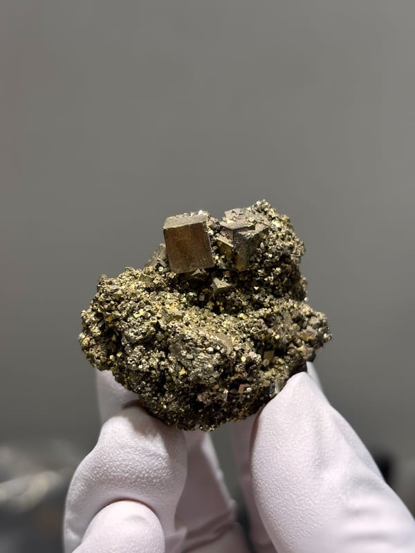 Brassy pyrite cubes on granular pyrite base from Hunan, China, held in gloved hand