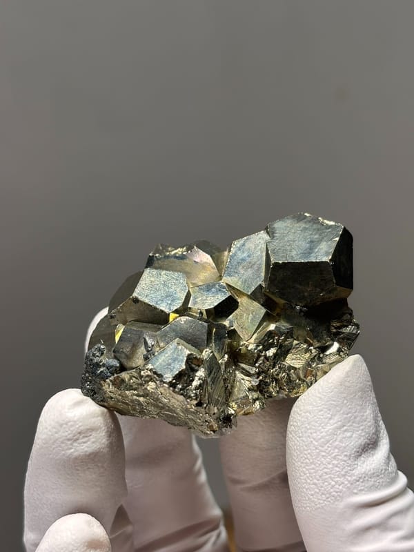 Brassy pyrite cube cluster from Indonesia, held in gloved hand