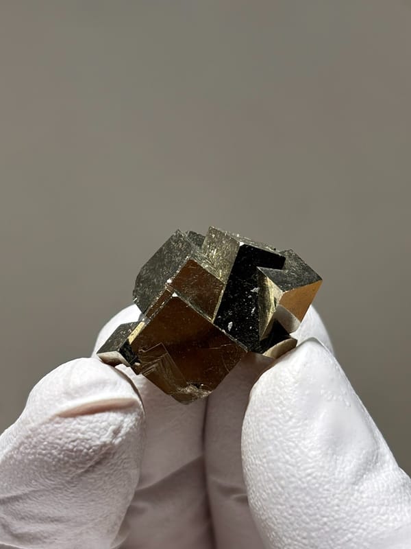 Tiny cluster of intergrown pyrite cubes from Hubei, China, held in gloved hand