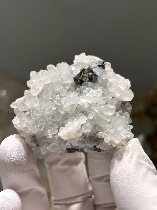 White quartz druse with pyrite and galena from Jiangxi, China, held in gloved hand