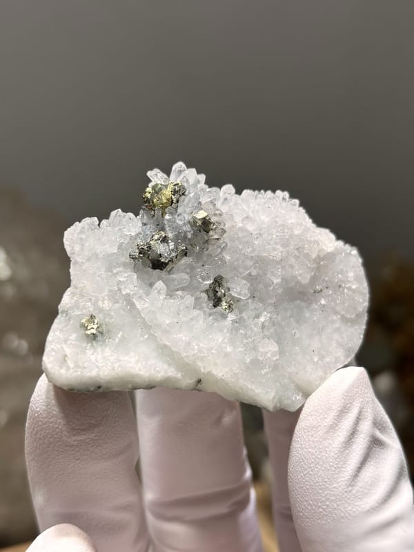 White quartz druse with pyrite and chalcopyrite from Jiangxi, China, held in gloved hand