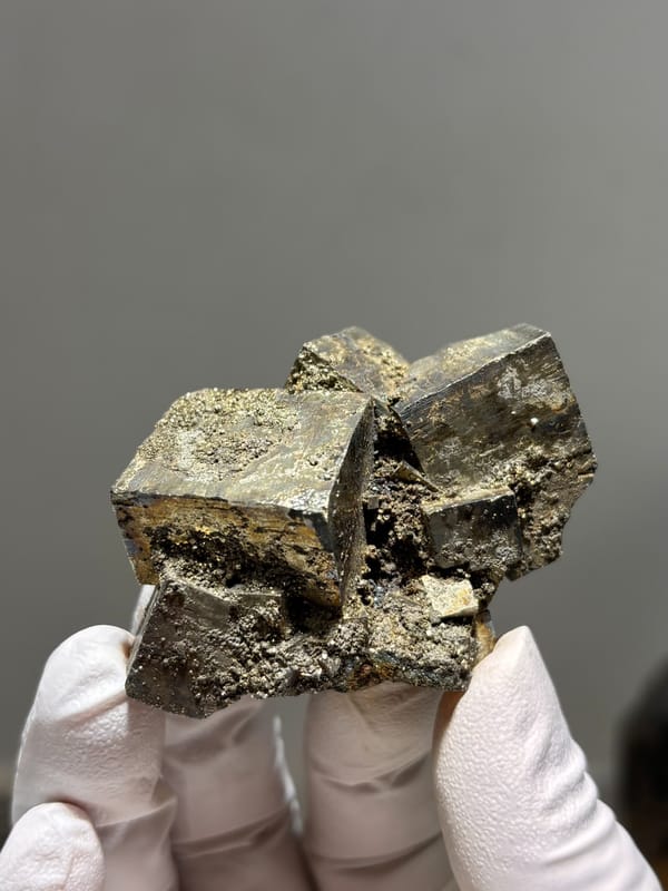 Cluster of pyrite cubes with mirror faces from Hubei, China, held in gloved hand