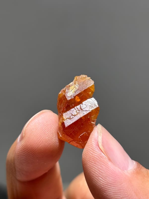 Tiny bright orange scheelite crystal from Xuebaoding, Sichuan, China, held in hand
