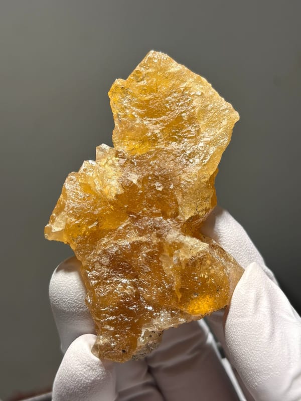 Golden scheelite crystal group from Xuebaoding, Sichuan, China, held in gloved hand
