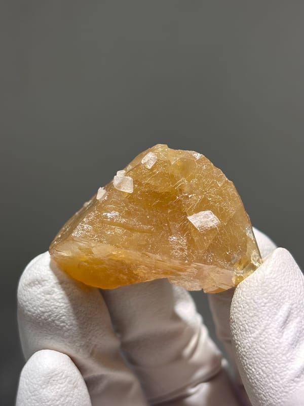Honey scheelite with white calcite specks from Xuebaoding, Sichuan, China, held in gloved hand