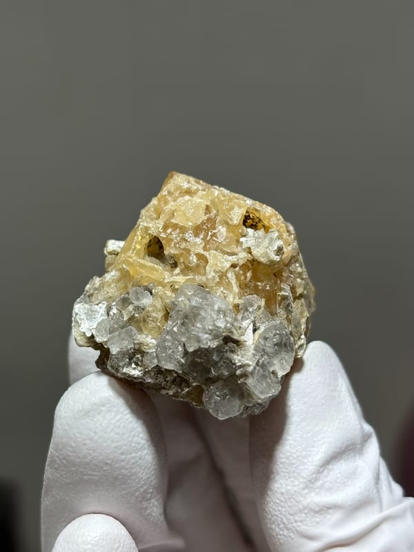 Honey scheelite with clear fluorite from Xuebaoding, Sichuan, China, held in gloved hand