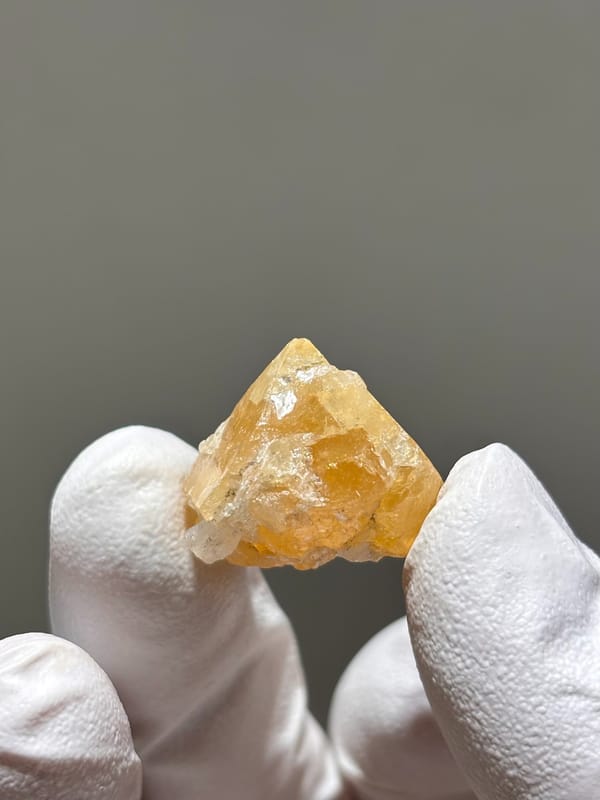 Small honey scheelite crystal with mica from Xuebaoding, Sichuan, China, held in gloved hand