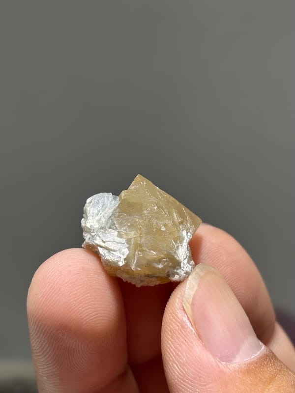 Small honey scheelite with mica from Xuebaoding, Sichuan, China, held in hand