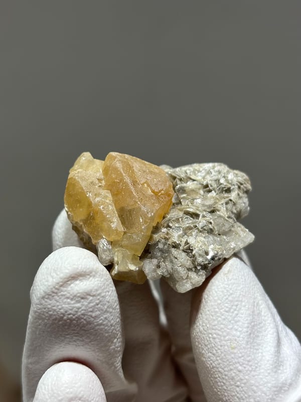 Honey scheelite crystal on mica with calcite base from Xuebaoding, Sichuan, China, close-up of the crystal faces