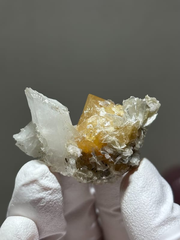 Honey scheelite with clear quartz point and mica from Xuebaoding, Sichuan, China, held in gloved hand