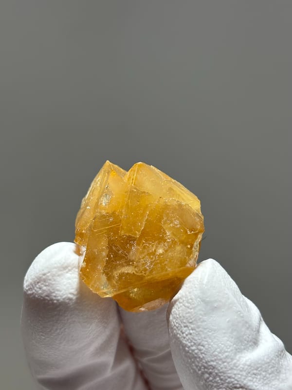 Honey scheelite crystal from Xuebaoding, Sichuan, China, held in gloved hand