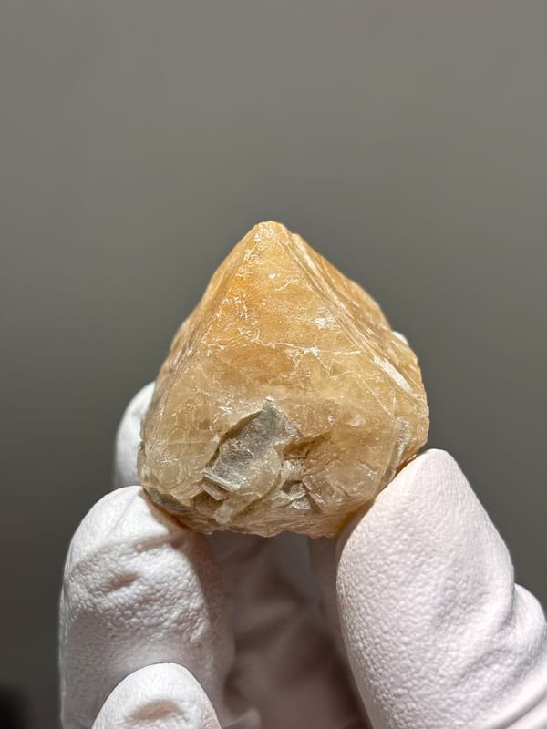 Honey scheelite with small fluorite from Xuebaoding, Sichuan, China, held in gloved hand