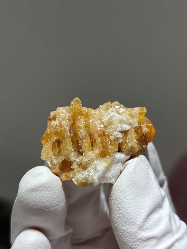 Honey scheelite in partly columnar habit from Xuebaoding, Sichuan, China, held in gloved hand