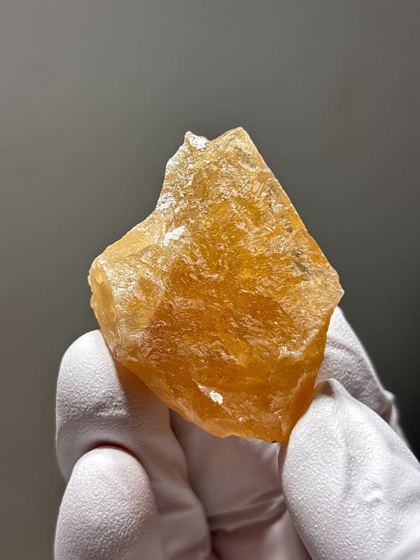 Honey-orange scheelite crystal from Xuebaoding, Sichuan, China, held in gloved hand