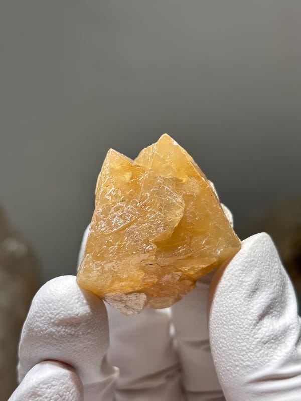 Honey-orange scheelite crystal group from Xuebaoding, Sichuan, China, held in gloved hand
