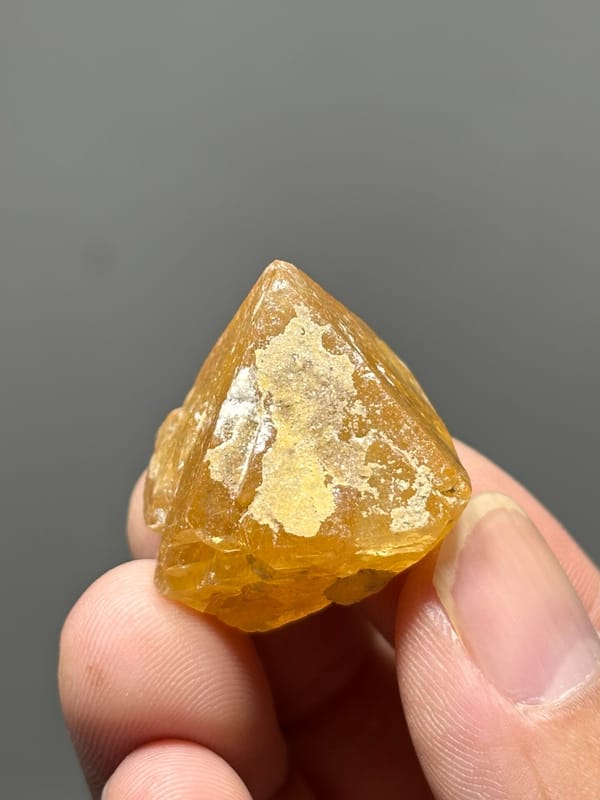 Orange scheelite crystal with white calcite from Xuebaoding, Sichuan, China, held in hand