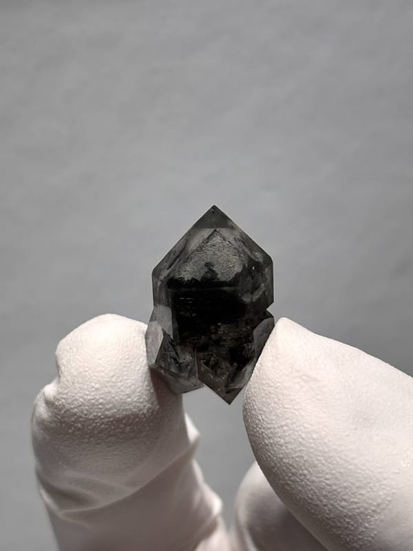 Stout black double-terminated quartz with clear cap from Yunnan, China, held in gloved hand