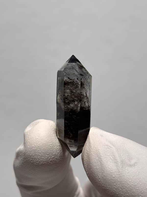 Black double-terminated quartz with clear tip from Yunnan, China, held in gloved hand