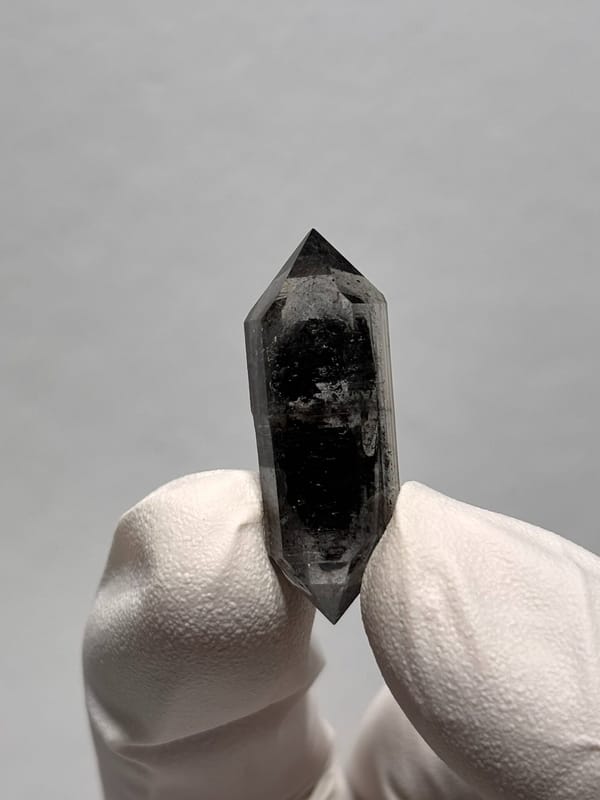 Black double-terminated quartz with clear rim from Yunnan, China, held in gloved hand