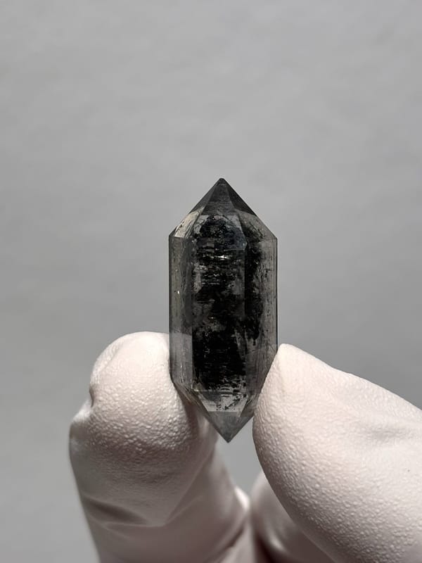 Black double-terminated quartz with clear rim from Yunnan, China, held in gloved hand