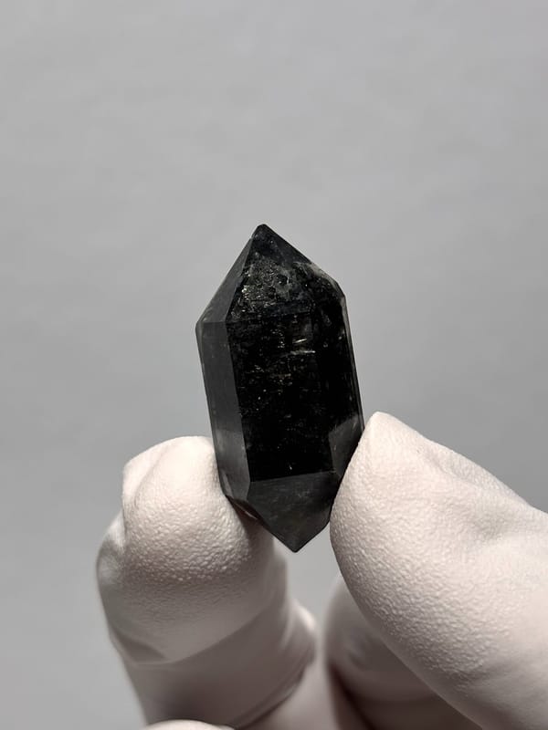Stout black double-terminated quartz with sparkles from Yunnan, China, held in gloved hand