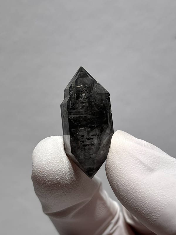 Stout black double-terminated quartz with sparkles from Yunnan, China, held in gloved hand