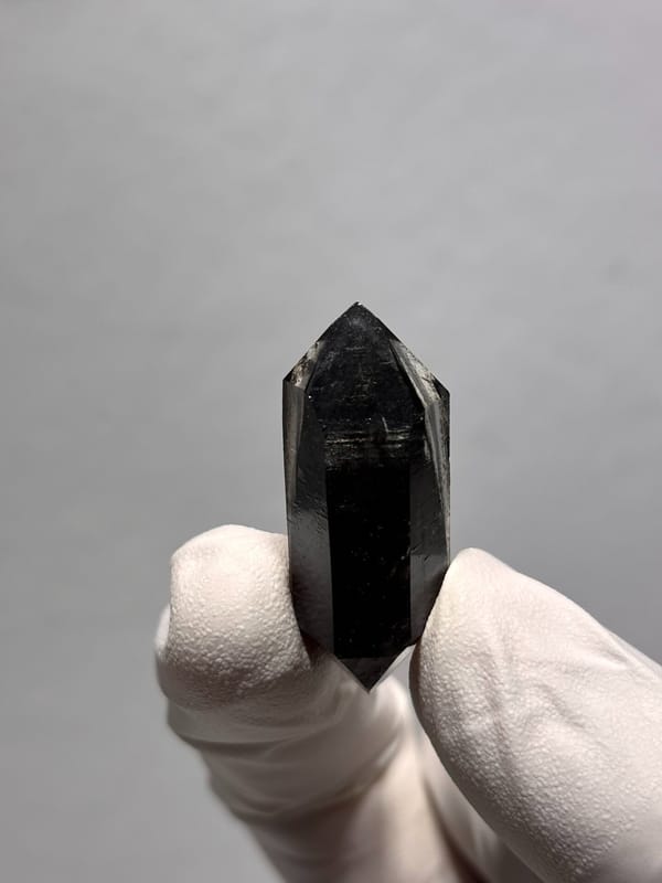 Stout black double-terminated quartz from Yunnan, China, held in gloved hand