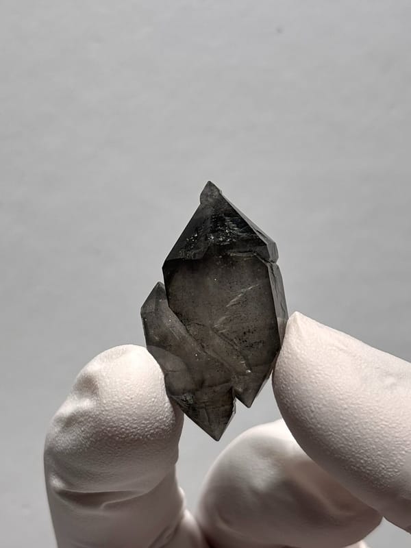 Black double-terminated quartz pair from Yunnan, China, held in gloved hand