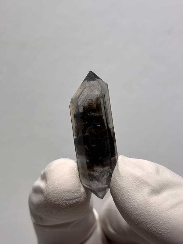 Black double-terminated quartz with clear tip from Yunnan, China, held in gloved hand