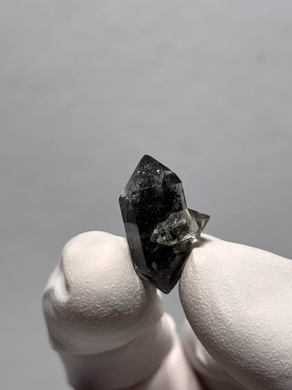 Tiny black double-terminated quartz with side crystal from Yunnan, China, held in gloved hand