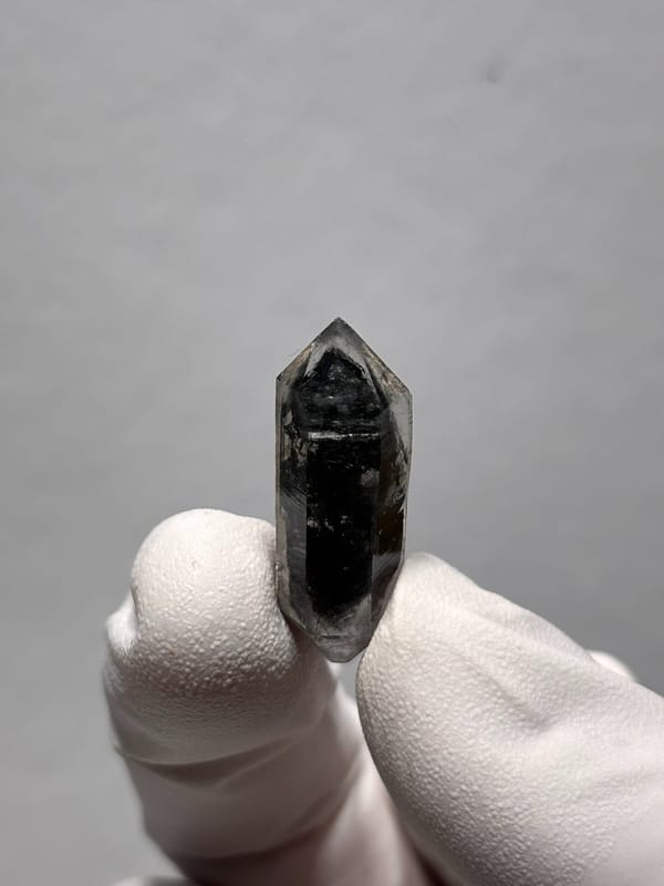 Tiny black double-terminated quartz with clear rim from Yunnan, China, held in gloved hand