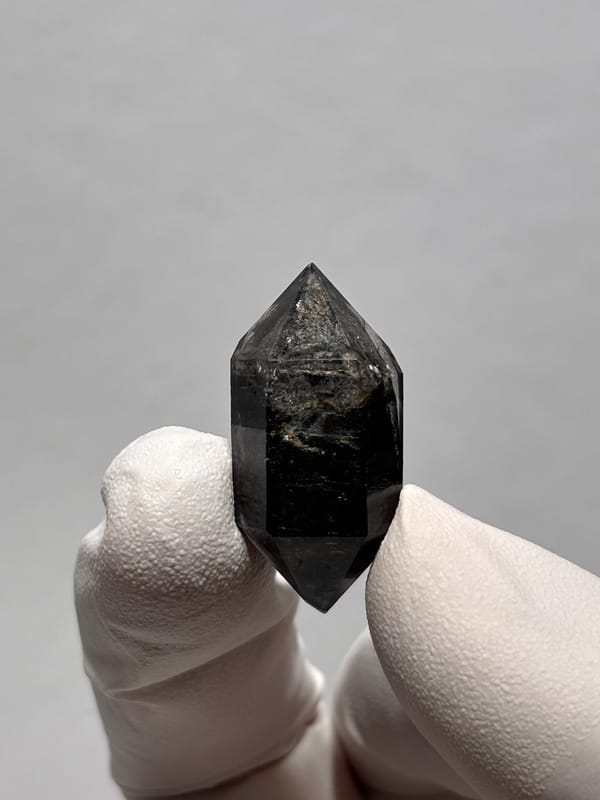 Stout black double-terminated quartz from Yunnan, China, held in gloved hand