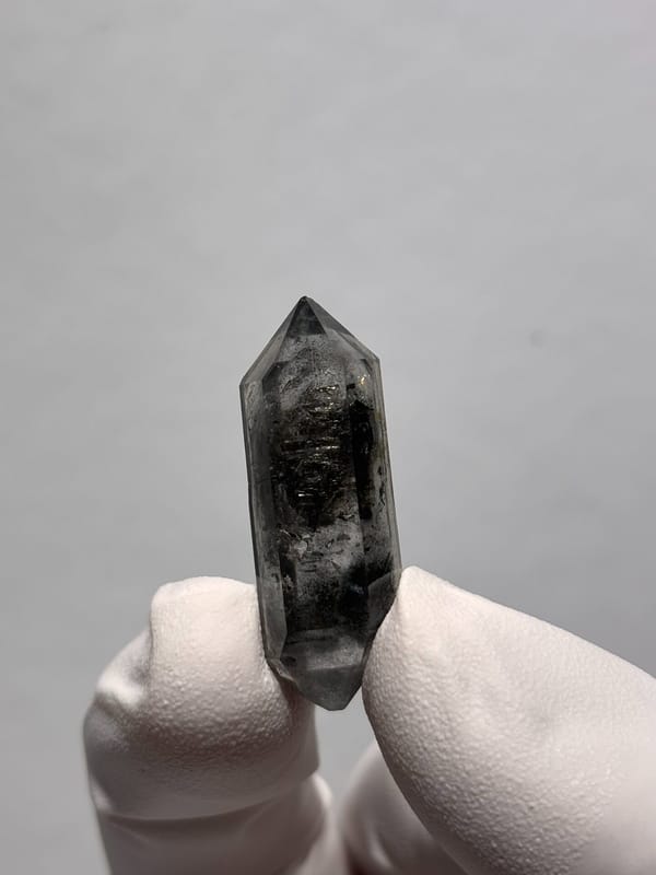 Black double-terminated quartz with clear tip from Yunnan, China, held in gloved hand