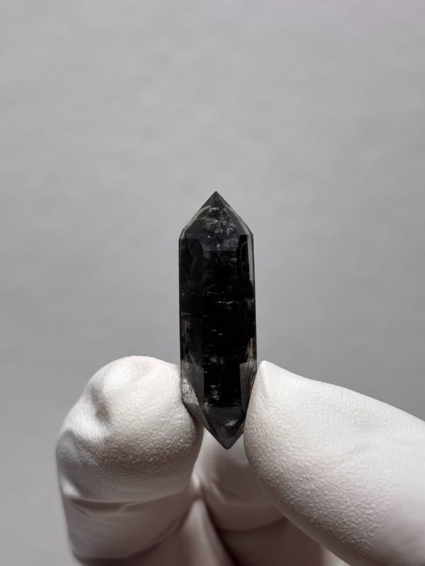 Tiny black double-terminated quartz from Yunnan, China, held in gloved hand