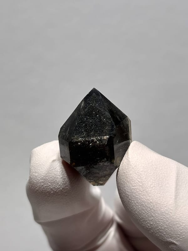 Black sparkly quartz with self-healed tip from Yunnan, China, held in gloved hand